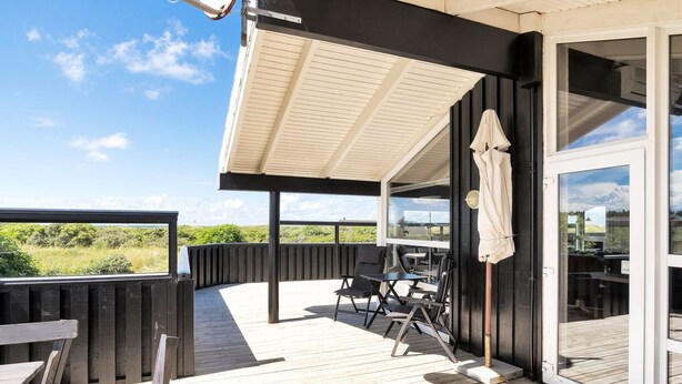 Una terraza de madera con mobiliario exterior, un espacio de estar cubierto y una puerta de vidrio que da a una habitación.