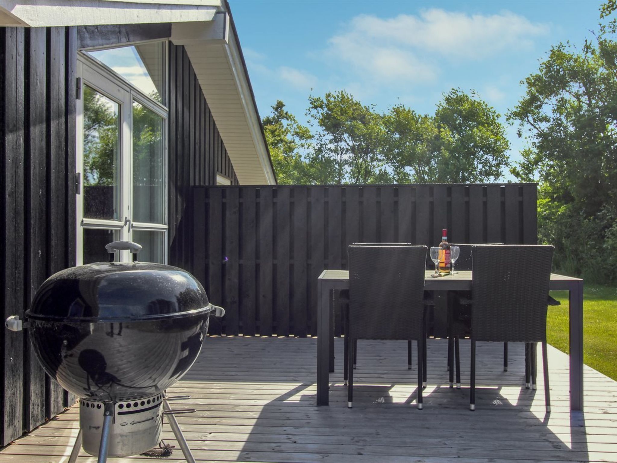 A wooden deck with a barbecue grill, a table, and chairs.