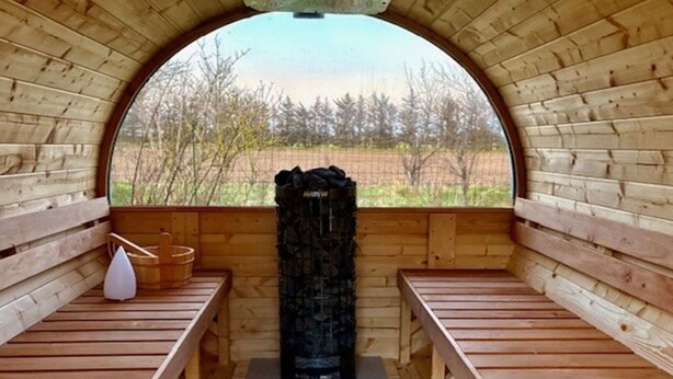 Una sauna con bancos de madera y una gran piedra volcánica negra en el centro.