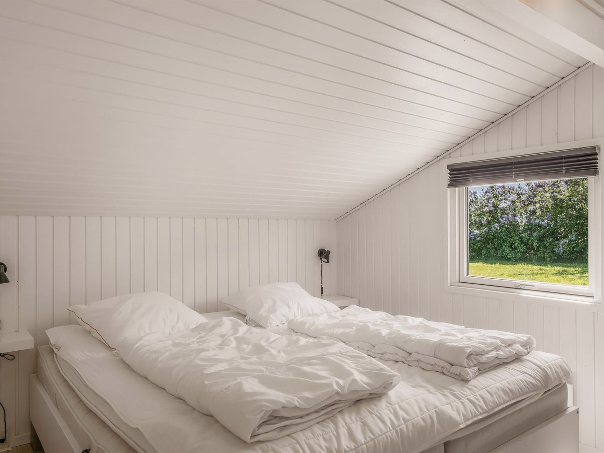 Une chambre à coucher avec un lit, une fenêtre donnant sur un paysage verdoyant et une lampe fixée au mur.