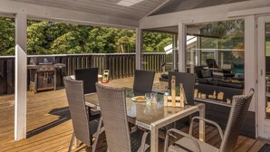 Eine Außenterrasse mit einer gläsernen Veranda, Korbmöbeln, einem Grill und einem Pool, der durch das Glas sichtbar ist.
