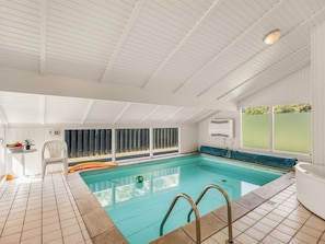 Ein Innenpool mit Fliesenboden, weißer Decke und einem Fenster mit Blick auf Grünflächen.