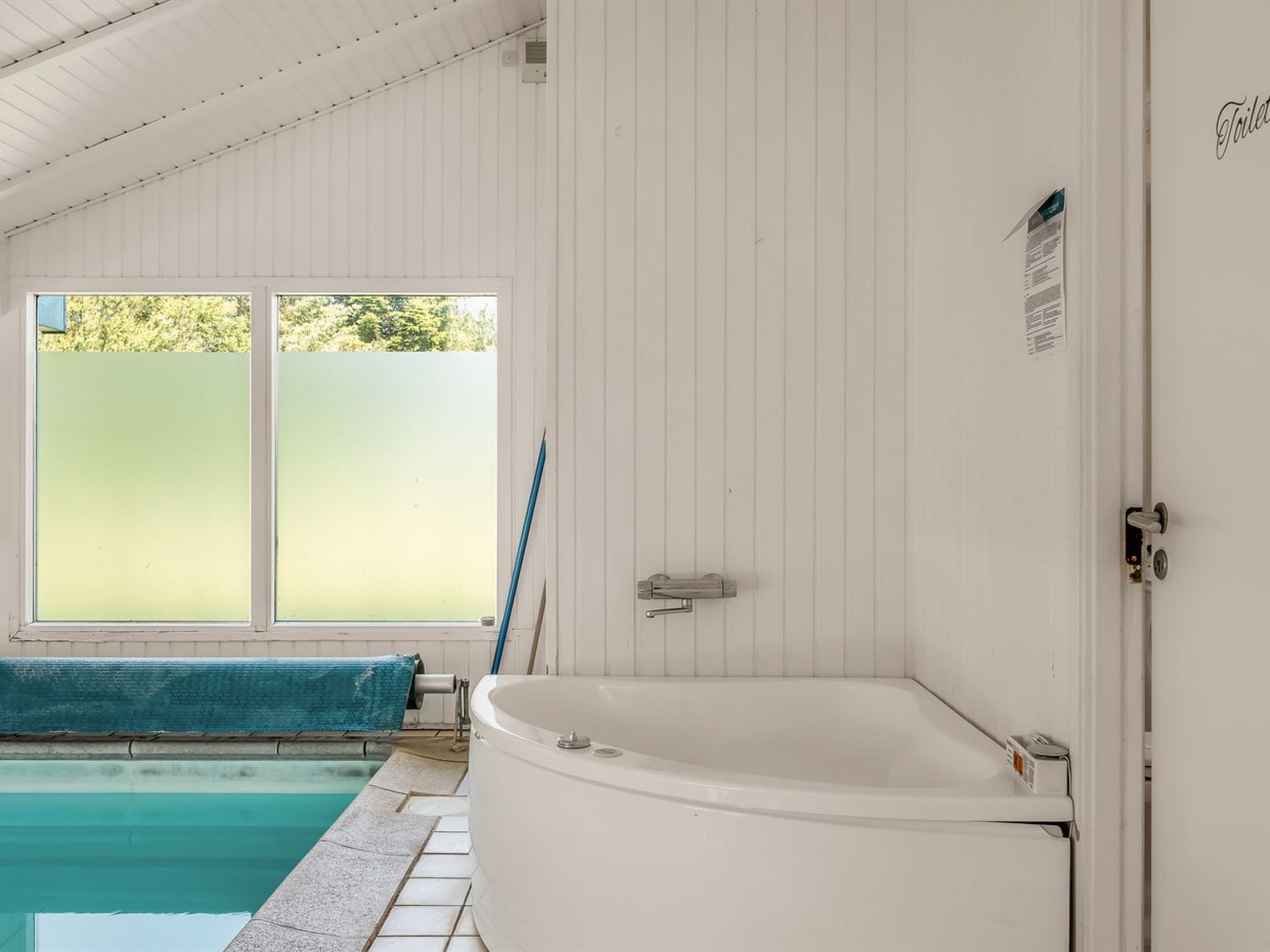 A bathroom with a white bathtub, a window with frosted glass, and a door with a sign.
