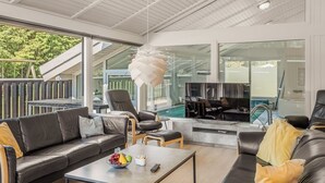 Ein modernes Wohnzimmer mit Sofa, Couchtisch und Fernseher, großen Fenstern und einem Pool, der durch die Scheiben sichtbar ist.