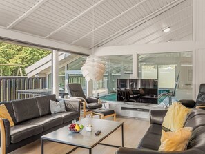 Ein modernes Wohnzimmer mit Sofa, Couchtisch und Fernseher, großen Fenstern und einem Pool, der durch die Scheiben sichtbar ist.