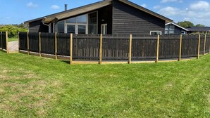 Ein modernes Haus mit dunkler Fassade, großen Fenstern und einem eingezäunten Garten.