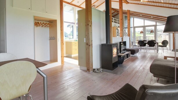 Ein geräumiger Raum mit hoher Decke, Holzbalken, Kamin, Essbereich und großen Fenstern.