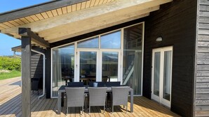 Ein überdachter Außenbereich mit Tisch und Stühlen, großen Fenstern und einer Holzterrasse.