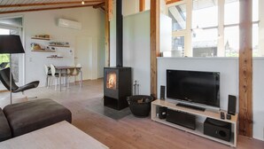 Ein modernes Wohnzimmer mit großem Fernseher, Kamin, Holzbalken und Essbereich.