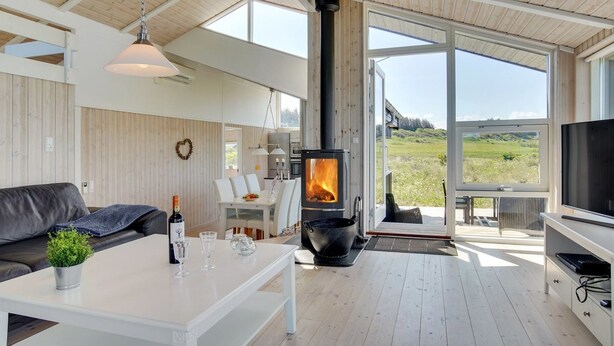 Un salon moderne doté d’une grande cheminée, d’un plancher en bois et de grandes fenêtres offrant une vue sur l’extérieur.