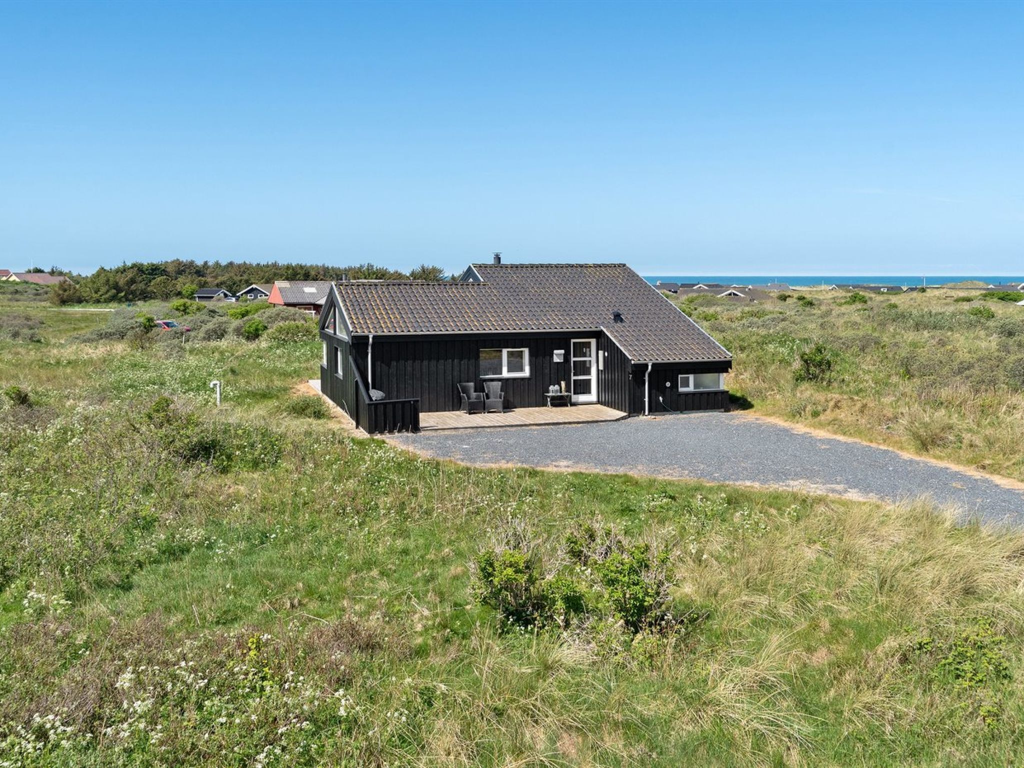Une maison noire avec une allée en gravier, un petit porche et une vue sur la mer.