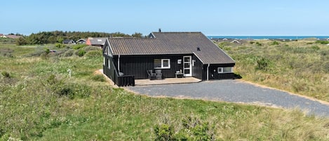 Une maison noire avec une allée en gravier, un petit porche et une vue sur la mer.