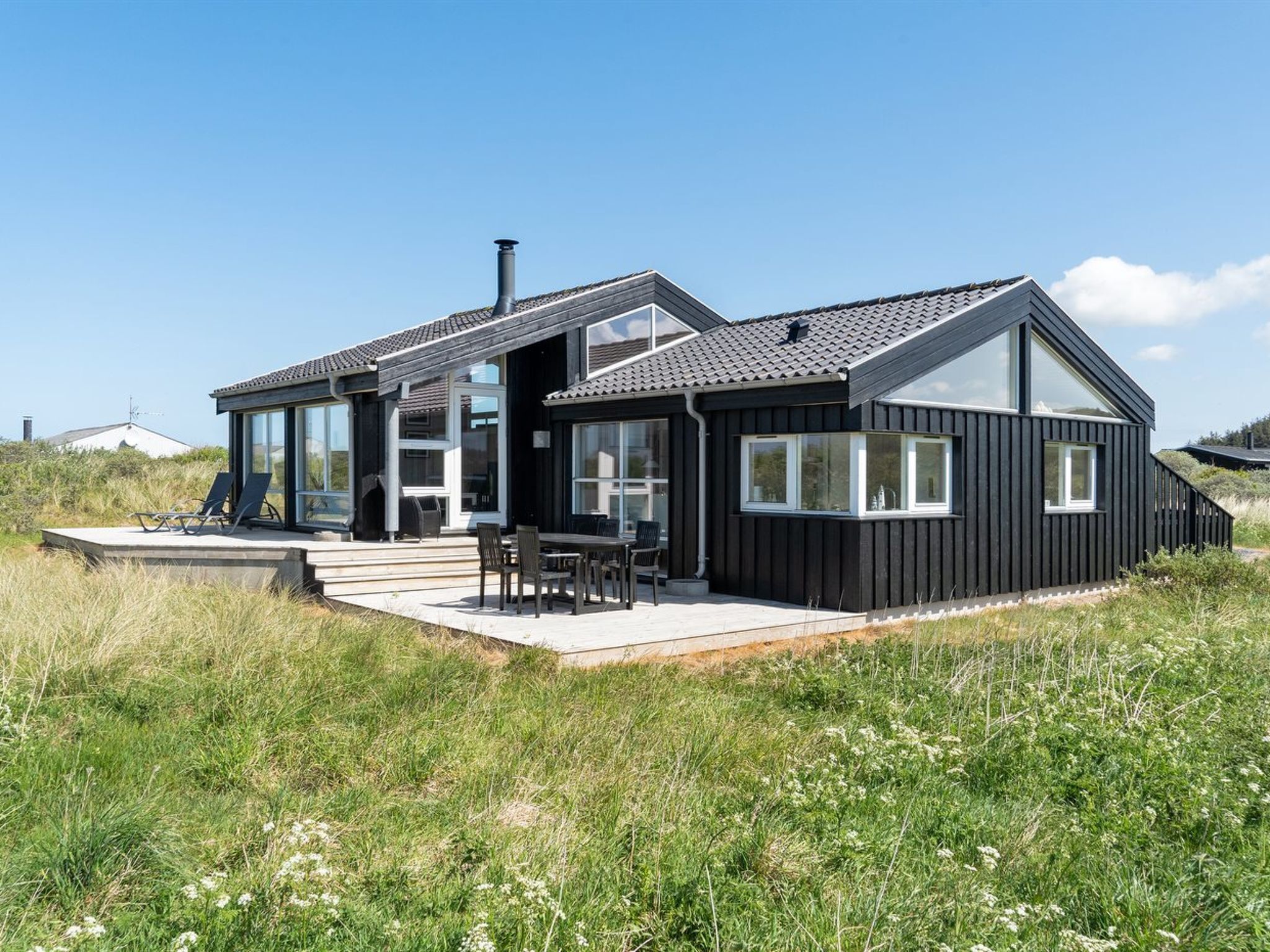 A modern black house with a deck, large windows, and a chimney.