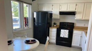 Una cocina compacta con armarios blancos, un refrigerador negro, una estufa y una mesa de comedor con sillas.