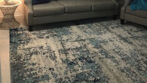 Una sala de estar con un sofá color beige, un tapete estampado y decoración en la pared, incluyendo un letrero que dice 'hello' y una escena de playa.