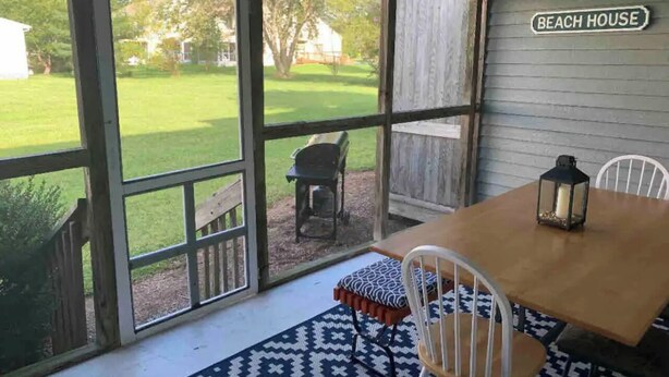 Un porche techado con una mesa y sillas de madera, un farol y vistas a un jardín con césped.