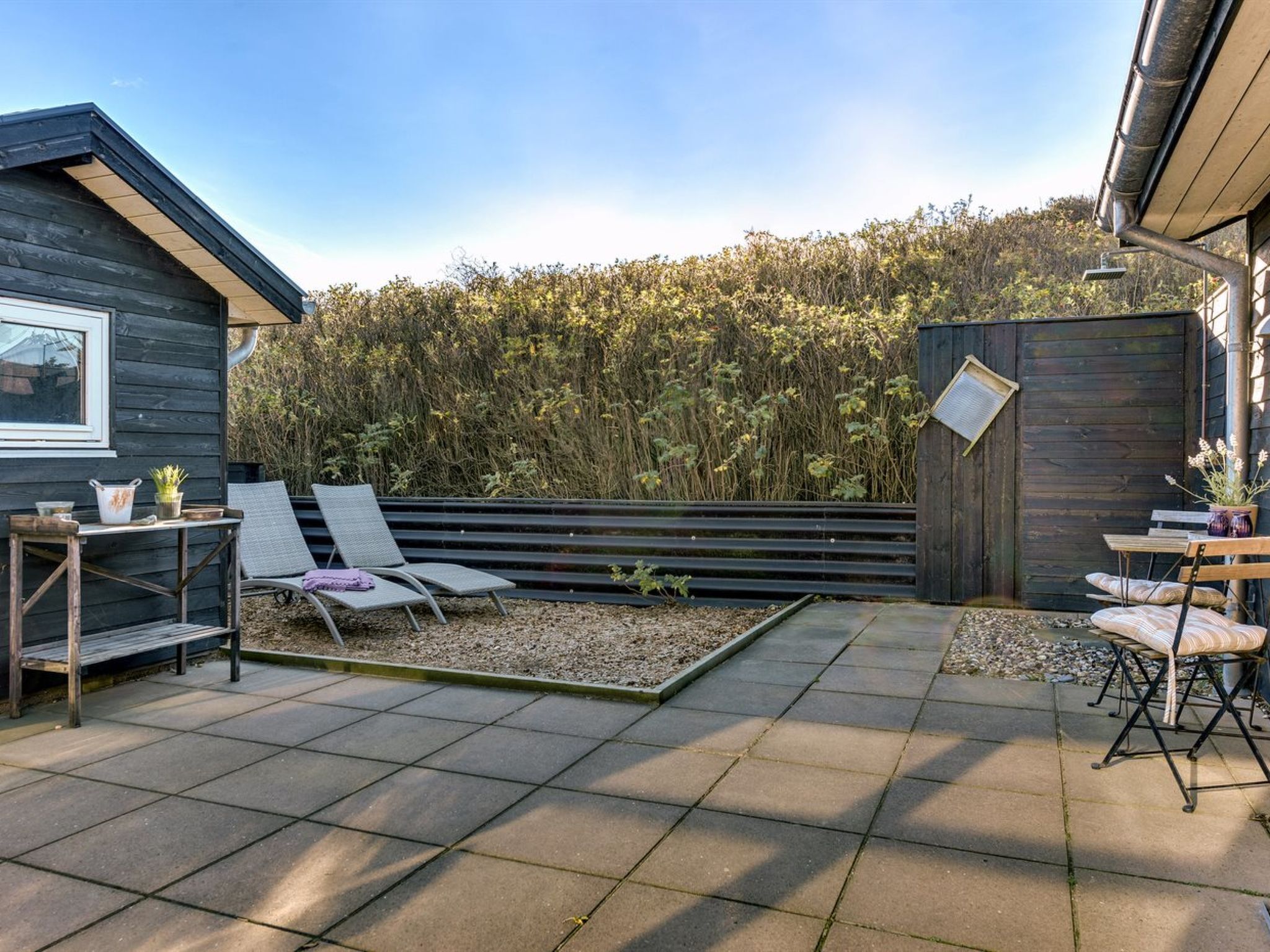 Une terrasse avec deux chaises longues, une petite table et une clôture en bois.
