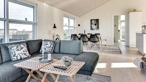 En moderne stue med en grå sofa, to træsofaborde og et spiseområde med et bord og stole.