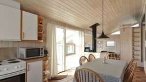 A compact kitchen with a stove, microwave, and wooden cabinets. There is a dining table with chairs and a large window providing natural light.