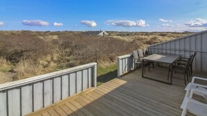 A wooden deck with a table and chairs, overlooking a landscape with sparse vegetation and distant houses.