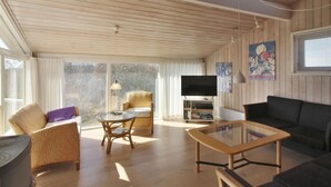 A spacious living room with wooden walls, a large TV, a sofa, a coffee table, and a chair.