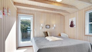 Een slaapkamer met een groot bed, een witte stoel, houten wanden en een raam.