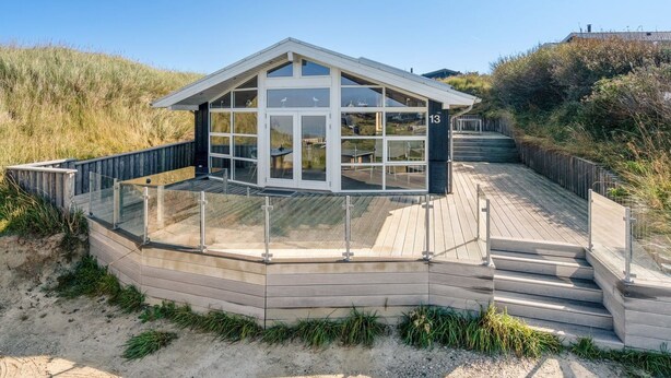 Een strandhuis met een glazen omheining, een houten terras en een bord met nummer 13.