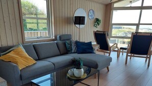 Een moderne woonkamer met een grijze bank, blauwe en gele kussens, een glazen salontafel en houten vloeren.