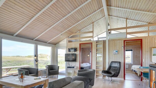 A spacious living area with a high ceiling, wooden beams, a large sofa, a television, and a view of the outdoors.