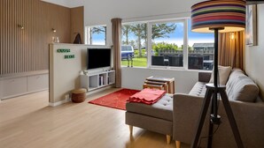 A modern living room with a flat-screen TV, a sofa, a coffee table, a lamp, and a view of the outside. - "Aarthi" - 637m from the sea by Interhome (Hjørring)