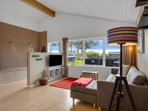 Una sala de estar moderna con televisor de pantalla plana, sofá, alfombra roja, lámpara y vistas al exterior.