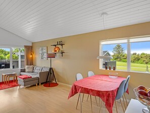 Une pièce comprenant un canapé, une table à manger avec des chaises, un lampadaire et une fenêtre donnant sur un paysage verdoyant.