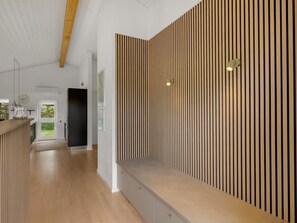 Un interior moderno con un muro de listones de madera, un banco y un pasillo que conduce a una puerta.