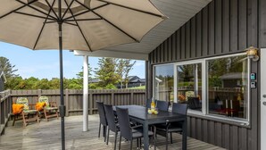 A covered outdoor deck with a table and chairs, a large umbrella, and a view of the backyard. - "Aarthi" - 637m from the sea by Interhome (Hjørring)