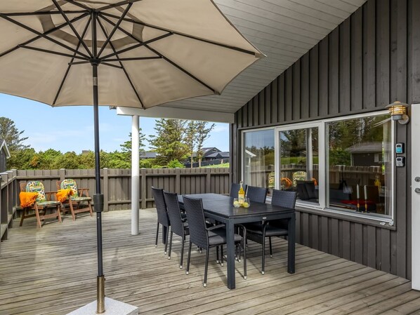 A covered outdoor patio with a table and chairs, a large umbrella, and a view through a window.