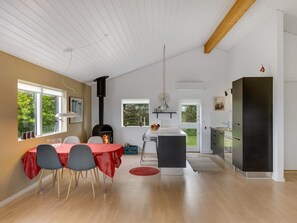 Una cocina moderna con un refrigerador negro, una zona de comedor con una mesa roja y un ventanal con vistas a zonas verdes.