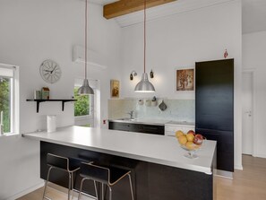A modern kitchen with a central island, pendant lights, and a clock on the wall.