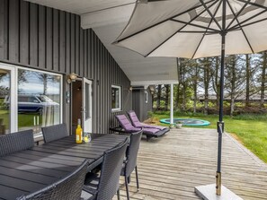 Un patio al aire libre con una mesa, sillas, un gran paraguas y un trampolín al fondo.