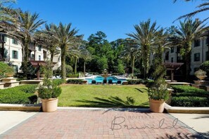 A hotel courtyard with palm trees, a swimming pool, and a brick pathway.