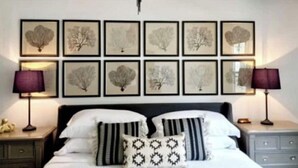 Ein Schlafzimmer mit einem Bett, zwei Nachttischen, einer Chandelierleuchtre und gerahmten botanischen Drucken an der Wand.
