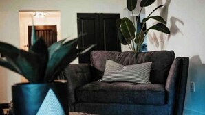 Ein Wohnzimmer mit einem dunkelgrauen Sofa, einem gestreiften Kissen und einer großen, grünen Pflanze im blauen Topf.