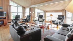 Un vaste salon avec des boiseries, des canapés en cuir, une table basse en verre et un téléviseur posé sur un meuble en bois.