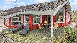 Un bâtiment rouge et blanc avec un toit en pente, une terrasse dotée de chaises longues et une table avec des chaises.