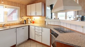 Une cuisine moderne avec des meubles en bois, des plans de travail en granit, un four encastré et une fenêtre équipée de stores.