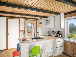 Une cuisine moderne avec un plafond en bois, des armoires blanches, un évier et une fenêtre donnant sur un jardin.