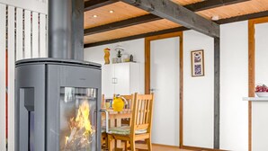 Un intérieur moderne avec un poêle à bois, un coin repas comprenant une table et des chaises en bois, et un meuble blanc.