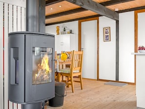 A modern interior with a wood-burning stove, a dining area with a wooden table and chairs, and a white cabinet.