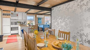 Une cuisine moderne avec des appareils électroménagers blancs, une table à manger en bois et une vue sur l’extérieur.