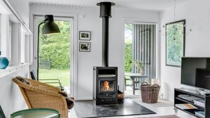 Una sala de estar moderna con una chimenea de leña, muebles de mimbre, un televisor y ventanas amplias.