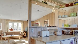 A cozy kitchen with a built-in refrigerator, a toaster, and a coffee machine. There is a dining area with a sofa and a table, and a window with curtains. - "Afrim" - 694m from the sea by Interhome (Hjørring)